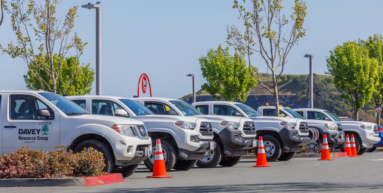 Fleet of utility trucks parked in an outdoor lot with safety cones and trees.