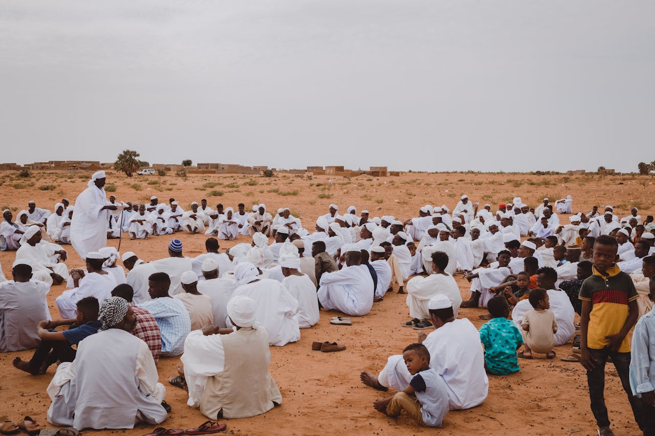 A large group of people in traditional white clothing gathered in a desert setting.