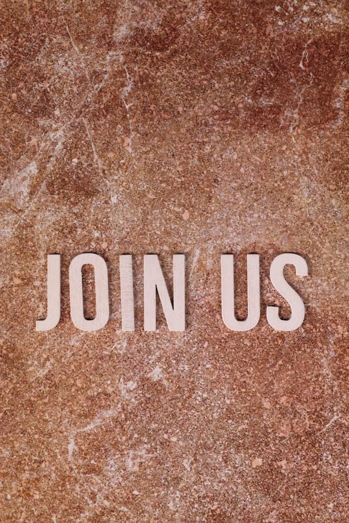 Flat lay of 'Join Us' text on a rustic stone background, inviting participation.